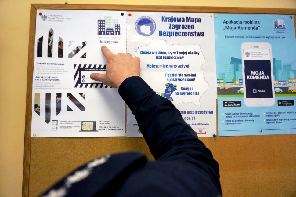 Obrazek przedstawia rękę umundurowanego policjanta, który wskazuje palcem na plakaty dotyczące akcji &quot;Dzielnicowy bliżej nas&quot; Krajowa mapa zagrożeń&quot; oraz aplikacja &quot;Moja komenda&quot;.