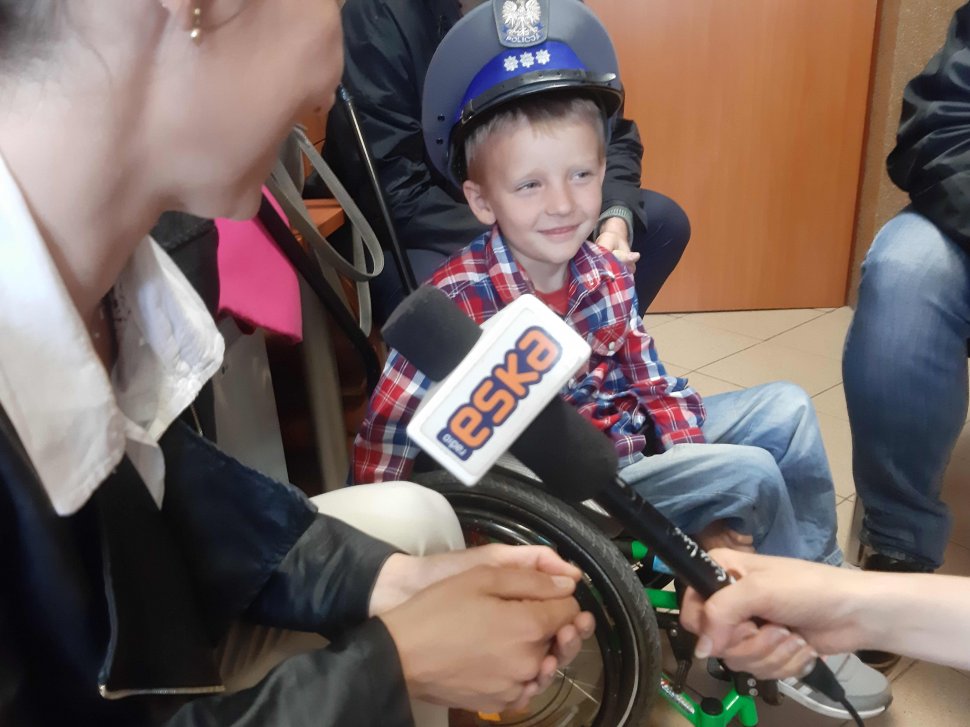 Zdjęcie przedstawia 6-letniego Jasia na wózku inwalidzkim wypowiadającego się do radia eska, widoczny mikrofon i obrócona bokiem jego mama 