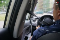 Obraz z wnętrza samochodu, widać policjanta w mundurze siedzącego na siedzeniu kierowcy i zapięte pasy