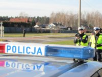 Obrazek przedstawia policjantów stojącym za radiowozem, którzy dokonują pomiaru prędkości