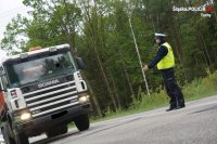 Obrazek przedstawia policjanta na drodze, który wskazuje kierującemu samochodem ciężarowym, ze ma się zatrzymać do kontroli