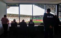 Obrazek przedstawia trzech umundurowanych policjantów i inne widoczne osoby w pomieszczeniu dowodzenia na Stadionie Miejskim w Tychach
