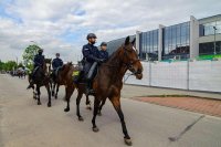 Obrazek przedstawia policjantów na koniach przechodzących obok stadionu