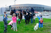 Obrazek przedstawia policjantów na koniach stojących przed stadionem, przed nimi dzieci