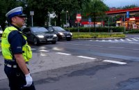 Obrazek przedstawia policjanta wydziału ruchu drogowego w białych rękawiczkach, który stoi bokiem w rejonie skrzyżowania