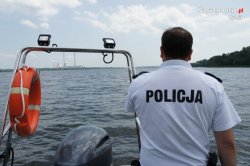 Obrazek przedstawia policjanta który płynie po jeziorze na motorówce