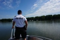 Obrazek przedstawia stojącego na łódce policjanta, który pływa po jeziorze