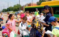 Obrazek przedstawia policjantkę rozdającą dzieciom kolorowanki, w tle stoi autobus