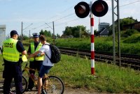 Obrazek przedstawia policjanta i sokistę rozmawiających z rowerzysta przy przejeździe kolejowym