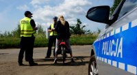 Na zdjęciu policjant ruchu drogowego i funkcjonariusze ochrony kolei rozmawiają z rowerzystkę, widoczny napis &quot;POLICJA&quot; z boku radiowozu