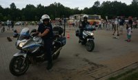 Na zdjęciu widoczni dwaj policjanci na motorze za nimi autobus oraz uczestnicy festynu