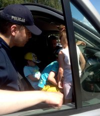 Wewnątrz samochodu widoczne dzieci, przy nich stoi umundurowany policjant