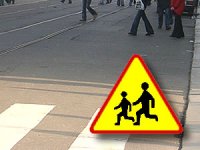 Zdjęcie przedstawia widok na rejon przejścia dla pieszych oraz znak drogowy na żółtym tle przebiegające dzieci koloru czrnego