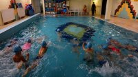 Dzieci pływają w wodzie na basenie pod nadzorem policjantki i dwóch ratowników WOPR