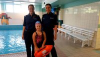 Dwie policjantki stoją na brzegu basenu wraz z dziewczynką, która trzyma bojkę pływacką.