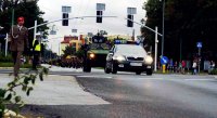 Policjant z drogówki w żółtej kamizelce zabezpiecza skrzyżowanie przez które przechodzi defilada z okazji obchodów Święta Wojska Polskiego, na przodzie jedzie policjant na motocyklu