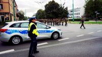Policjantka wydziału ruchu drogowego, stoi przy radiowozie i zabezpiecza defiladę z okazji obchodów Święta Wojska Polskiego.