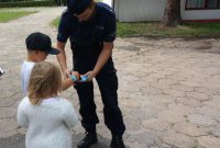 Policjant rozdaje opaski odblaskowe chłopcu i dziewczynce.