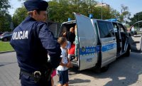 Na zdjęciu widoczny policjant, dalej dzieci, które znajdują się wewnątrz radiowozu.
