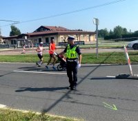Na zdjęciu widoczny policjant wydziału ruchu drogowego, w żółtej kamizelce, który kieruje ruchem podczas półmaratonu, z tyłu widoczne osoby.