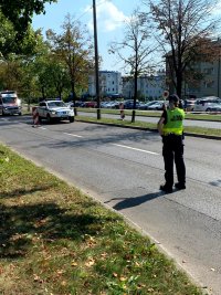 Na zdjęciu widoczna funkcjonariusza straży miejskiej, która stoi tyłem, dalej widoczny radiowóz oraz karetka pogotowia.
