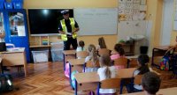 Na zdjęciu widoczny policjant wydziału ruchu drogowego w klasie, przed nim w ławkach siedzą dzieci.