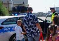 Na zdjęciu widoczny policjant, który pokazuje dzieciom i ich rodzicom radiowóz.