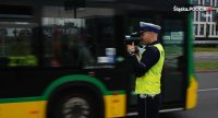 Na zdjęciu widoczny policjant, który mierzy prędkość pojazdów ręcznym miernikiem prędkości.