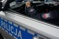Na zdjęciu widoczny przez okno radiowozu rękaw munduru policjanta z drogówki oraz bok radiowozu z napisem &quot;POLICJA&quot;.
