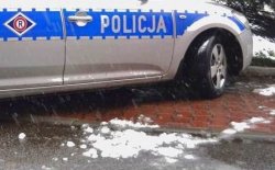 Widoczny bok radiowozu z napisem: &quot;Policja&quot;, na drodze śnieg.