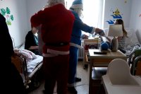 Na sali w oddziale dziecięcym szpitala mikołaje i policjant odwiedzają chore dzieci i rozdają prezenty.
