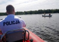 Umundurowany policjant na motorówce, w tle widoczna woda i dwie osoby na łódce.