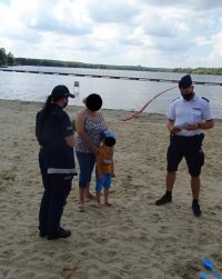 Umundurowani policjami rozmawiają z kobietą i dzieckiem podczas spotkania profilaktycznego na brzegu zalewu &quot;Paprocany&quot; .