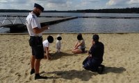 Policjanci rozmawiają z rodziną z dzieckiem wypoczywającą nad brzegiem wody.