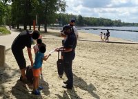 Policjanci rozmawiają z mężczyzną oraz dwójką dzieci o bezpieczeństwie nad wodą, przekazują kolorowanki dzieciom.