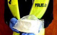 Policjant w żółtej kamizelce i rękawiczkach ochronnych trzyma w woreczku strunowym amfetaminę.