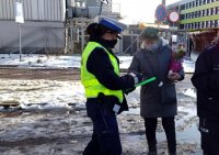 Policjantka Ruchu Drogowego przekazuje opaskę odblaskową kobiecie, która trzyma kwiaty w ręku.
