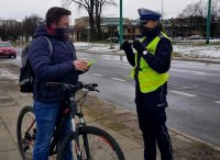 Policjantka rozmawia z rowerzystą i daje mu opaskę odblaskową.