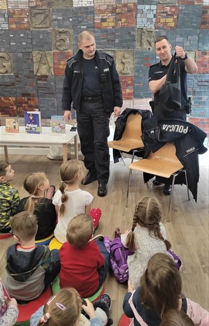 Na zdjęciu dwóch umundurowanych policjantów pokazujący dzieciom polar od munduru. Przed policjantami grupa dzieci w wieku przedszkolnym.