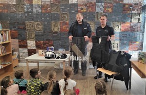 Na zdjęciu dwóch umundurowanych policjantów pokazujących dzieciom sprzęt do zabezpieczania imprez. Przed policjantami grupa dzieci w wieku przedszkolnym.