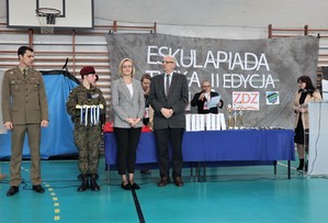 Na zdjęciu grupa osób zajmująca się wręczaniem nagród. Widać również stół, na którym rozłożone są medale, puchary oraz nagrody. W tle widać rozwieszony na drabinkach napis Eskulapiada Tyska II Edycja.
