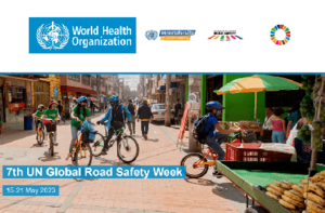 Na zdjęciu plakat promujący Światowy Tydzień Bezpieczeństwa Ruchu Drogowego. Na plakacie kilka osób na rowerze, z założonymi kaskami. Tło zdjęcie stanowi chodnik z zabudowaniami po obu stronach. Na górze plakatu logo organizacji, na środku plakatu napis 7th UN Global Road Safety Week 15-21 May 2023.