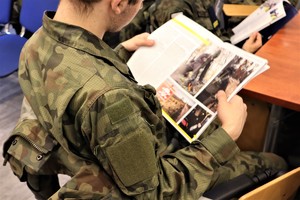Na zdjęciu uczeń w mundurze moro przeglądający gazetę policyjną.