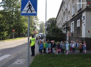 Na zdjęciu policjantka i grupa przedszkolaków przed przejściem dla pieszych.