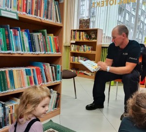 Na zdjęciu policjant czytający książkę dzieciom