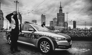 Na zdjęciu policjant stojący na baczność przy radiowozie