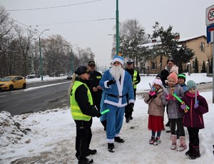 Na zdjęciu umundurowany policjant, strażnicy miejscy oraz Mikołaj podczas rozdawania odblasków.