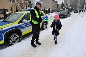 Na zdjęciu umundurowany policjant wręczający odblask dziecku