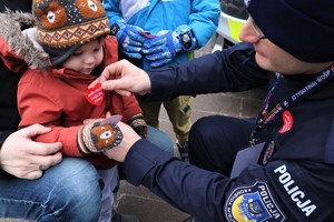 Na zdjęciu policjant przyklejający naklejkę dziecku podczas obchodów 32. Finału Wielkiej Orkiestry Świątecznej Pomocy.