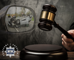 Zdjęciu przedstawiające sędziowski młotek oraz uszkodzony samochód widoczny w bocznym lusterku pojazdu.